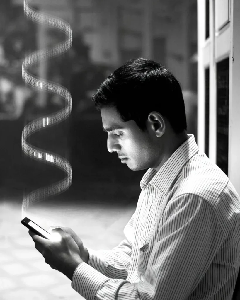 অন্ধকার ঘরে স্মার্টফোনের দিকে একদৃষ্টিতে তাকিয়ে থাকা এক ব্যক্তি, যা সোশ্যাল মিডিয়ায় অ্যালগরিদমের বৃত্ত, ডিজিটাল কারাগার এবং আমাদের পছন্দের বিভ্রমকে তুলে ধরে।