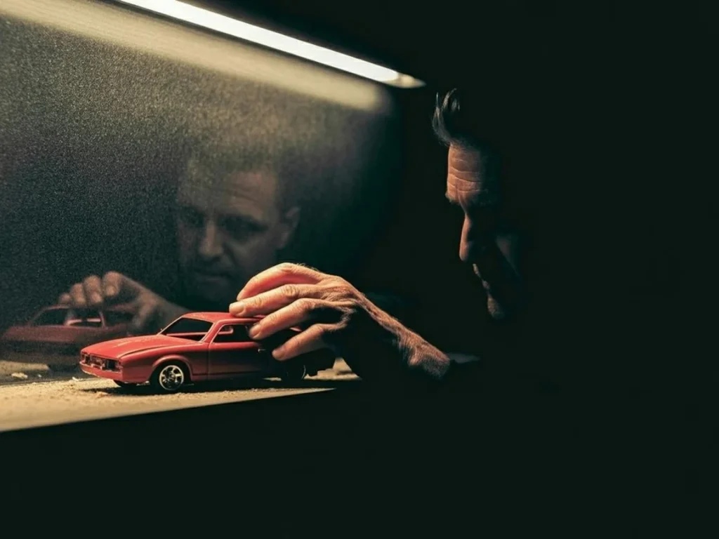 A man's hand touching a dusty red toy car symbolizing the loss of childhood innocence and the burden of growing up.