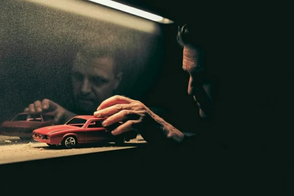 A man's hand touching a dusty red toy car symbolizing the loss of childhood innocence and the burden of growing up.