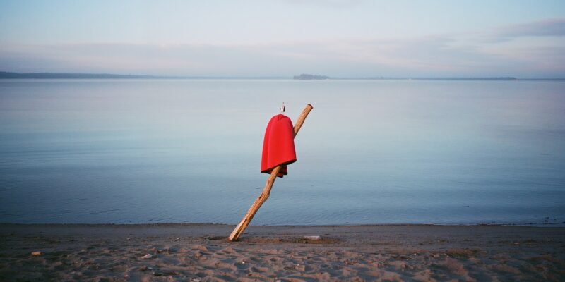 be your authentic self — a child’s towel-cape pinned to driftwood by a calm lakeshore at dawn