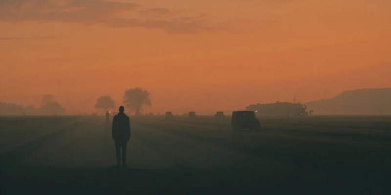 A figure experiencing absent grief walks alone at sunset, contemplating asymmetric mourning and generational loss across time