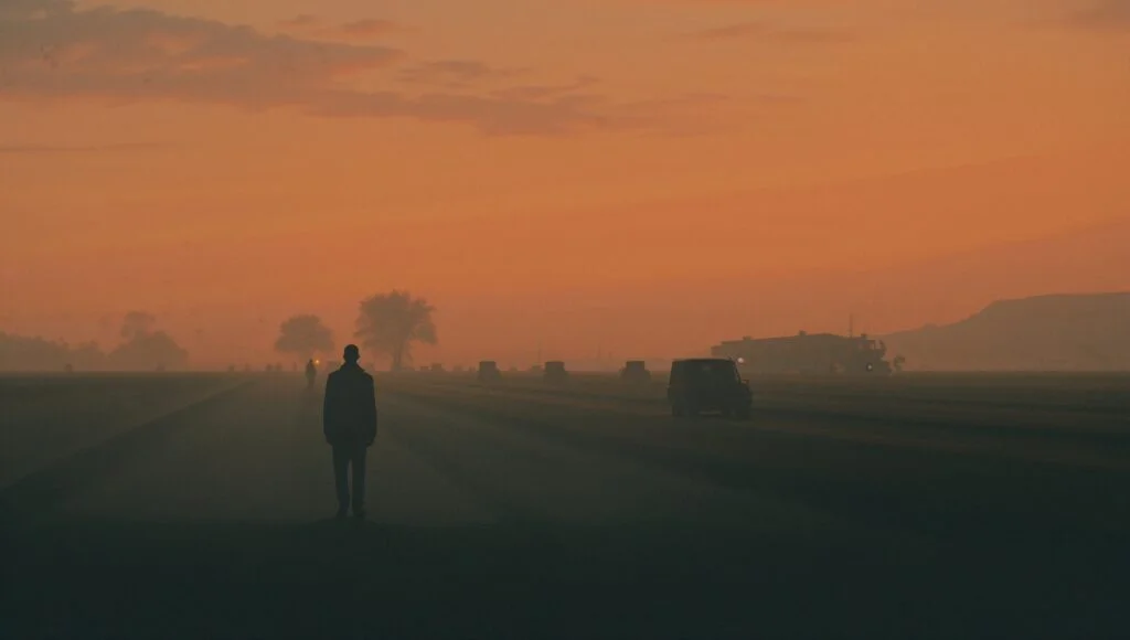 A figure experiencing absent grief walks alone at sunset, contemplating asymmetric mourning and generational loss across tim